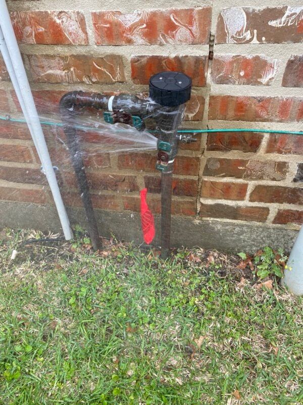 Brick wall with leaking water pipe, red-handled valve, grass below, black top component.