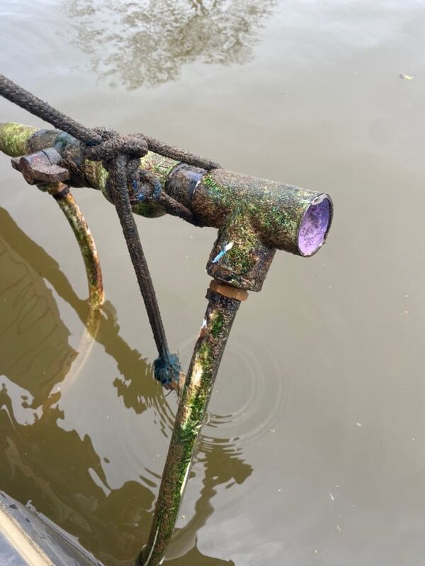 Aging metal pipe with moss, tied by rope, partially in murky water.