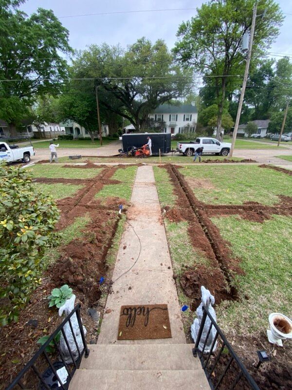 Front yard landscaping with trenches, workers, vehicles, trees, and houses; pathway and welcome mat.