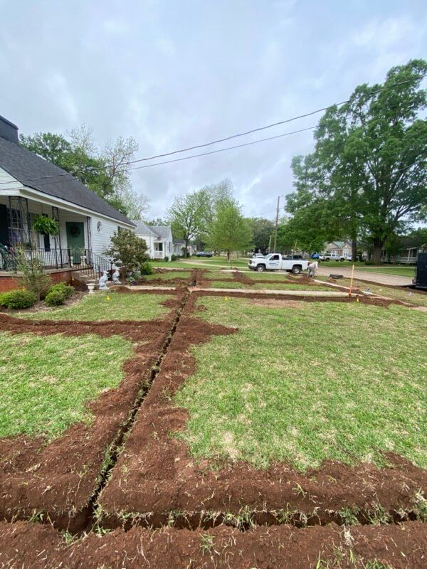 Residential area with dug trenches in lawn, white truck, trees, power lines, cloudy sky.